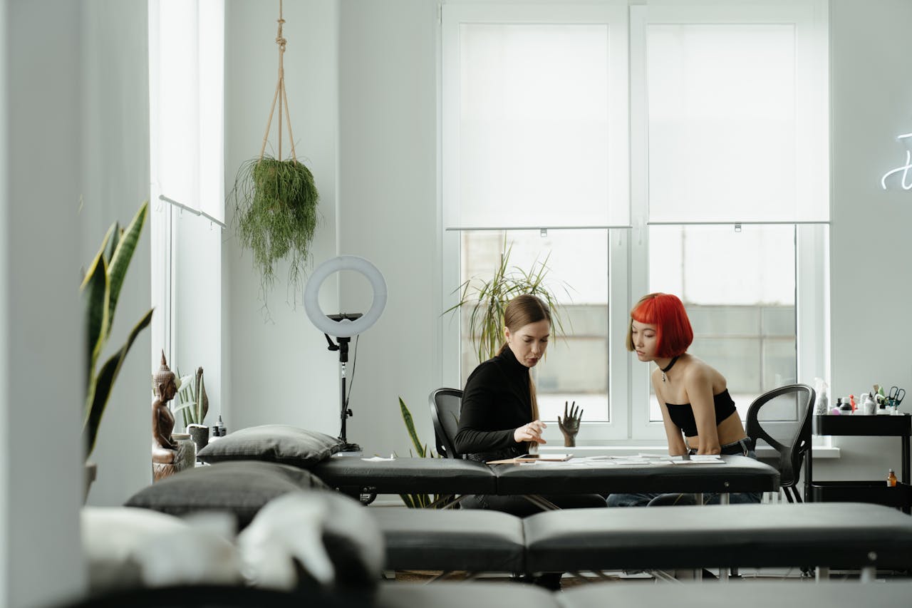 services-02 A tattoo artist and client collaborating in a stylish, well-lit studio with plants and modern decor.