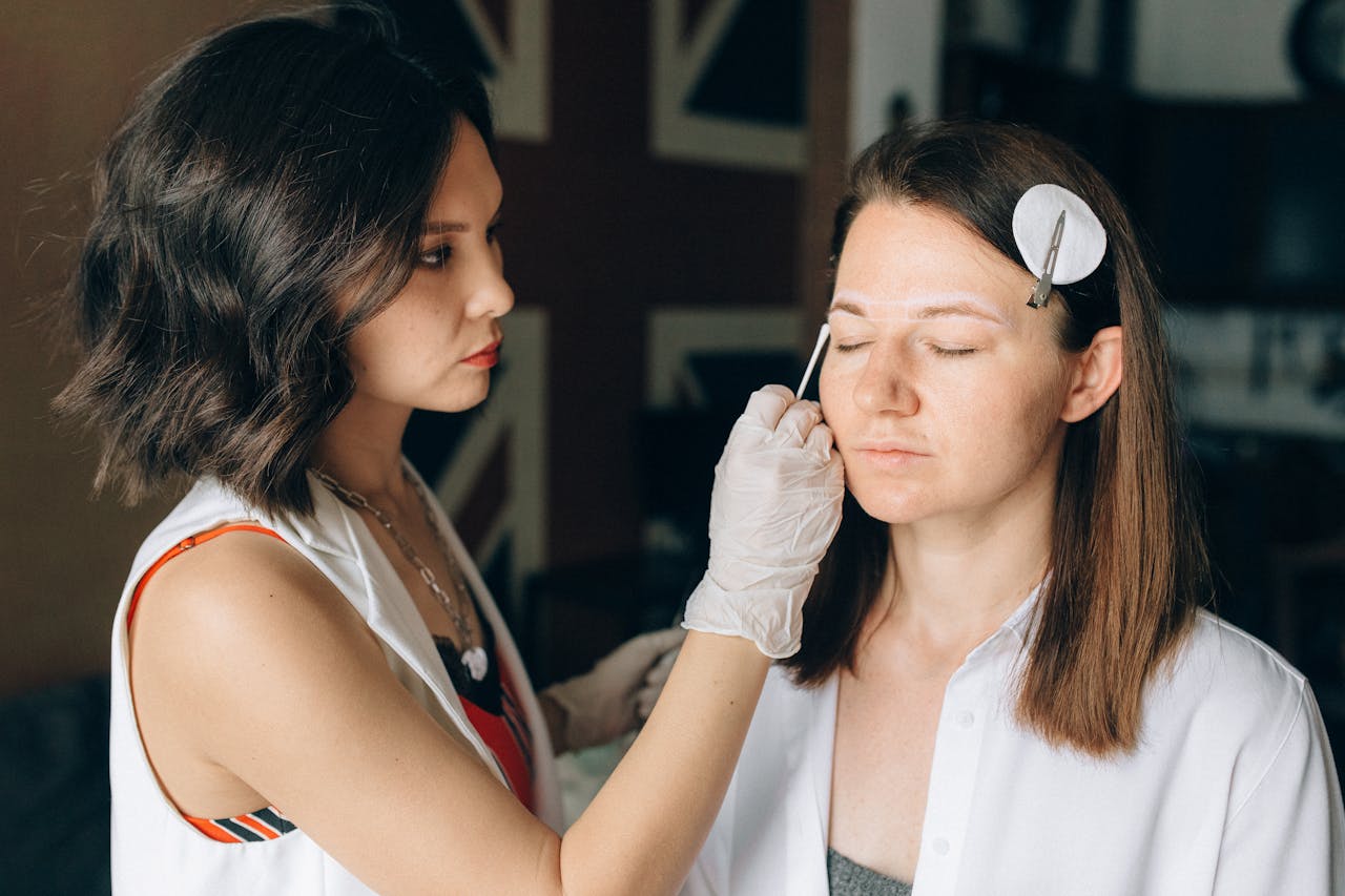 who-we-are A skilled makeup artist applies makeup to a client in a professional indoor setting.